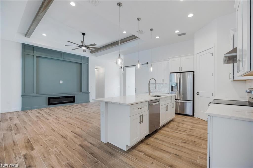 Kitchen featuring decorative light fixtures, an island with sink, white cabinets, and appliances with stainless steel finishes