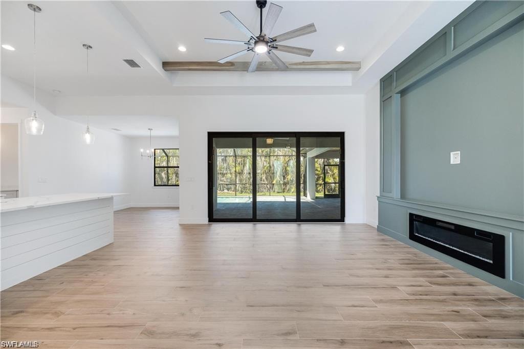 Unfurnished living room featuring ceiling fan with notable chandelier and light wood-type flooring