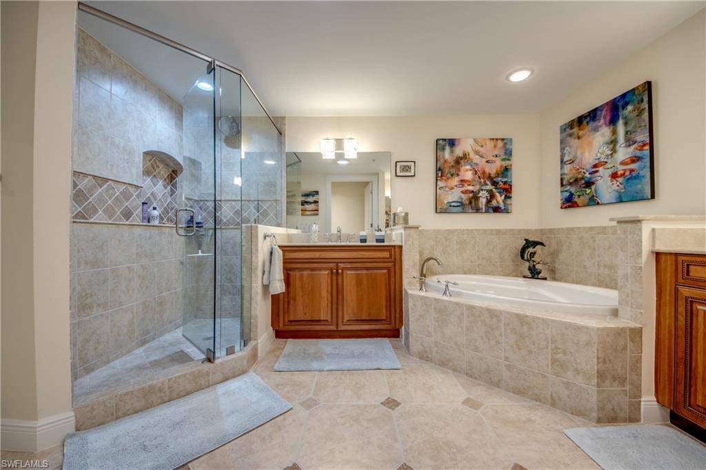 Spacious  master bathroom featuring a glass-enclosed shower with tile surround and integrated niche, a soaking tub with tiled base, wood-finish vanity with countertop, and large wall mirror
