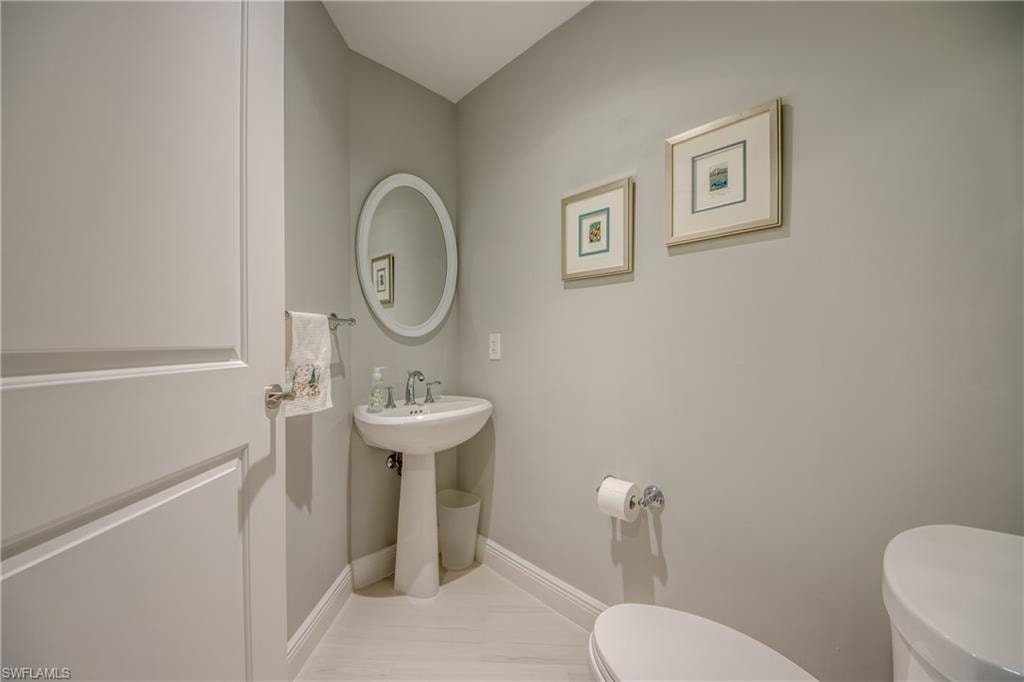 Pedestal sink, oval mirror, light-toned wood-finish flooring, and a paneled door with brushed nickel hardware