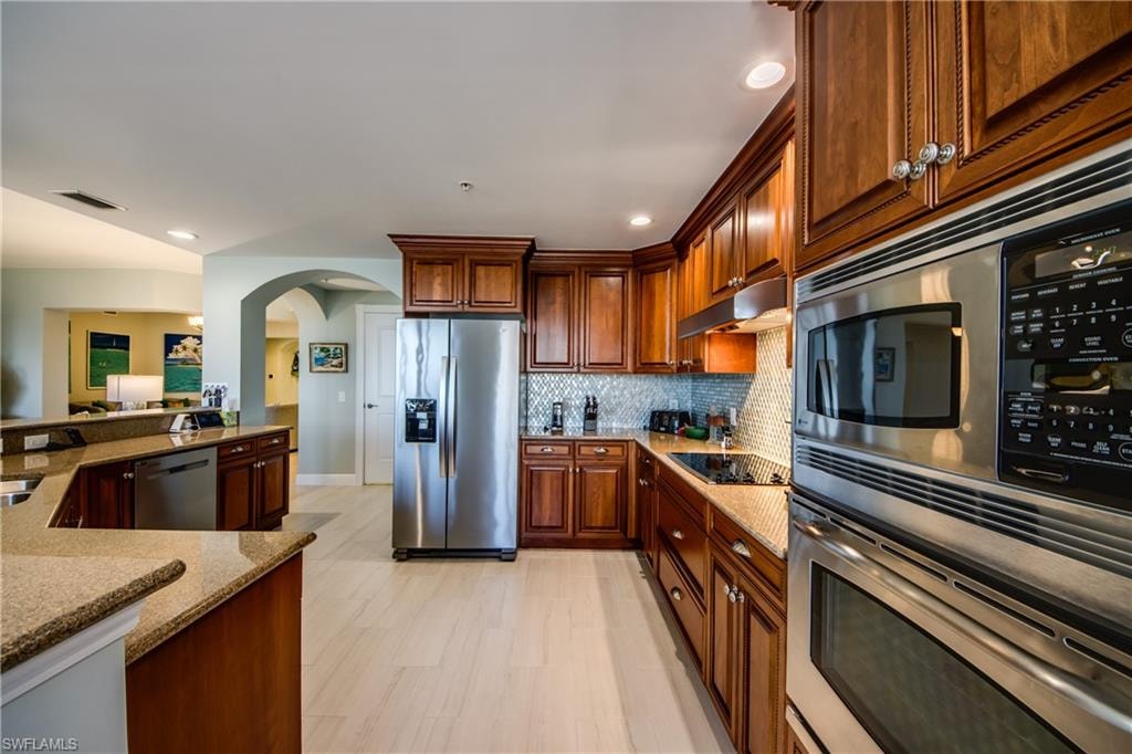 Gourmet kitchen featuring wood cabinetry, integrated stainless steel appliances, a tile backsplash, light wood-finish flooring, and a breakfast bar with stone countertops