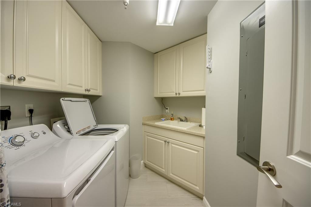 Dedicated laundry space featuring a white top-load washing machine and dryer, extensive upper and lower cabinetry, a built-in utility sink with counter space, and light-toned flooring