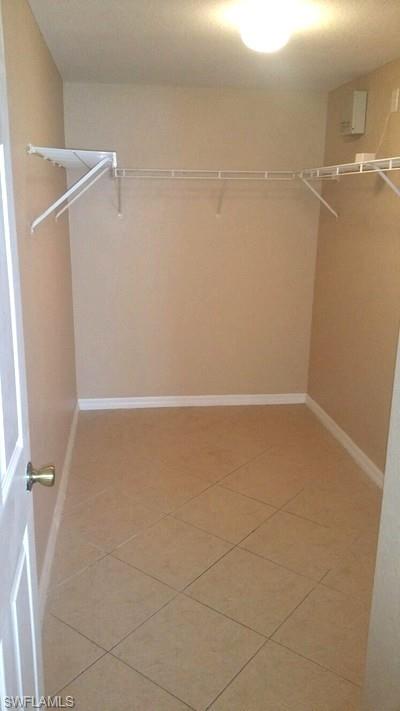 Spacious walk-in closet featuring tile flooring, dual wall-mounted clothing rods, and bright overhead lighting