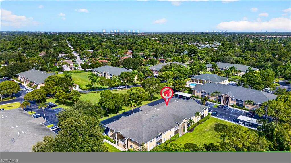 Aerial overview of a multi-building residential complex featuring mature landscaping, surface parking, and carports