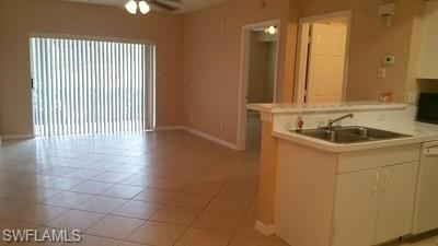 Tile flooring, ceiling fan, sliding glass doors, white kitchen cabinetry, and a double basin sink