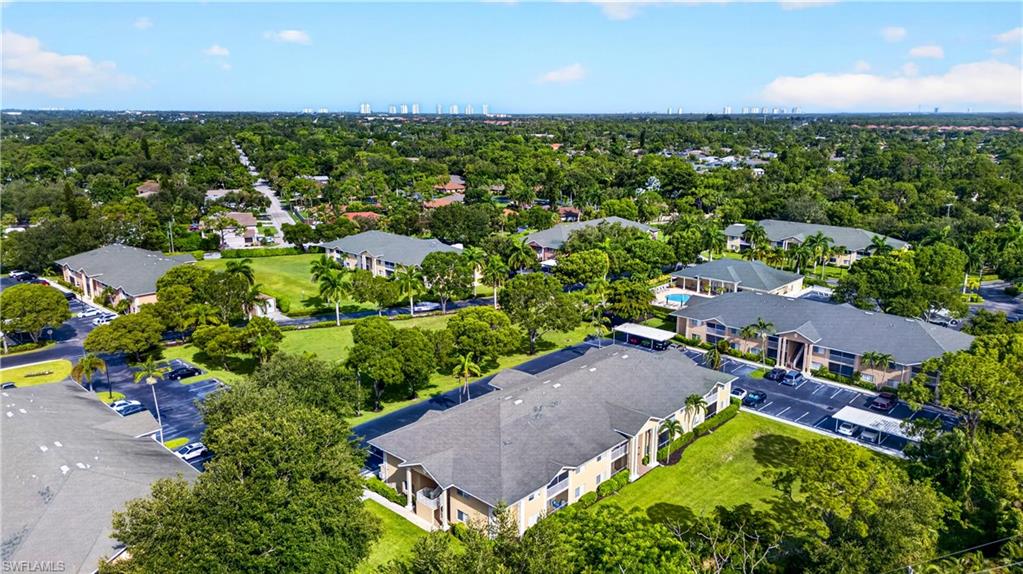 Aerial property view featuring multiple multi-story residential buildings with dark shingle roofs, surrounded by extensive green lawns and mature trees