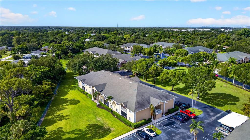 Multi-unit residential property featuring a light-colored exterior with dark shingle roofing, surrounded by lush green lawns and mature trees