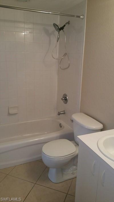 White tiled bathtub with a chrome shower fixture and a toilet with a white vanity