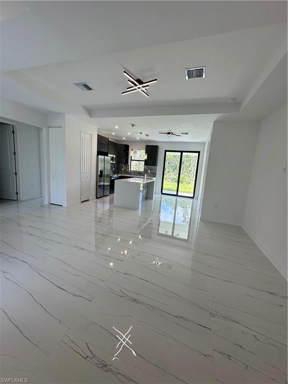 Expansive open-concept interior featuring large format marble-look tile flooring, contemporary ceiling light fixtures, and a tray ceiling