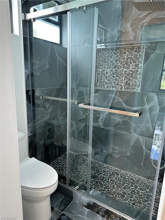 Spacious shower enclosure featuring dark marbled tile, a pebble-finish floor, a recessed wall niche with mosaic tile, and a square rain shower head