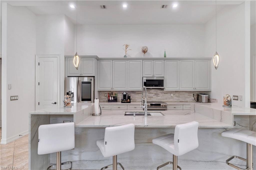 Spacious kitchen featuring a large island with waterfall edge, light-toned cabinetry, stainless steel appliances, a tiled backsplash, and recessed lighting
