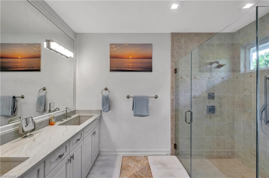 Bathroom featuring a dual vanity with undermount sinks and light-toned countertops, a full-width mirror, and a glass-enclosed shower with tiled walls and multiple shower heads