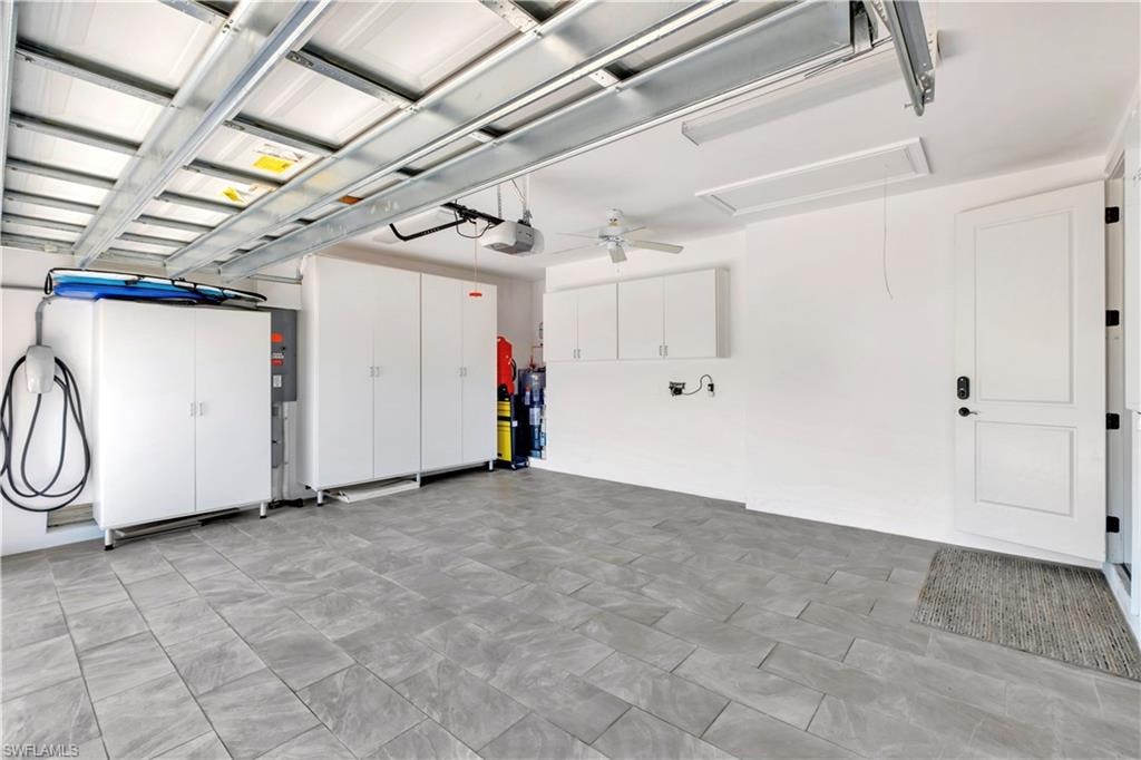 Spacious garage featuring large format gray tile flooring, extensive built-in white cabinetry, a ceiling fan, and an electric vehicle charging station