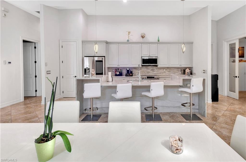 Kitchen featuring white cabinetry, a light-toned backsplash, stainless steel appliances, and a breakfast bar with seating