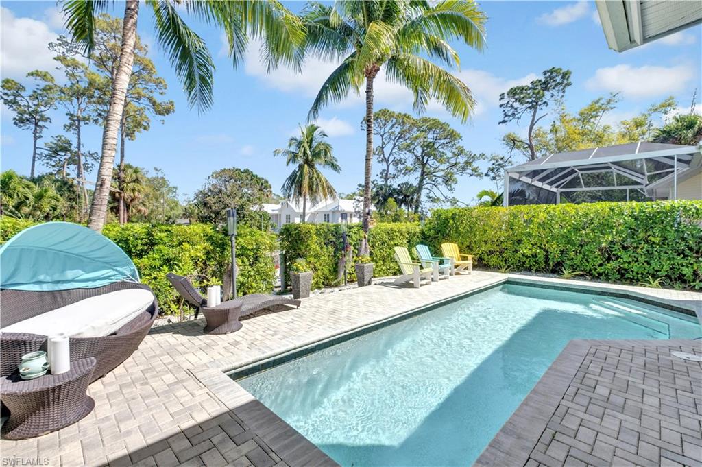 Outdoor pool area featuring a rectangular pool, paver decking, lush perimeter landscaping, and mature palm trees