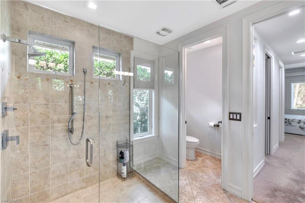 Spacious glass-enclosed shower featuring large format tile, dual shower heads, and multiple windows