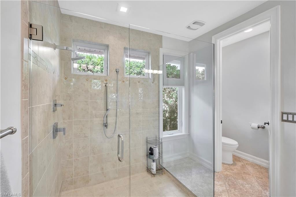Glass-enclosed shower featuring light-toned tilework with accent borders, multiple shower heads, and transom windows