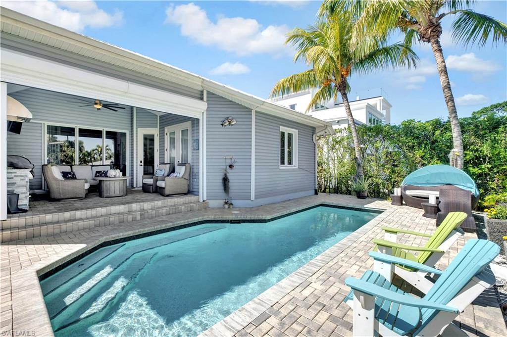 Paved patio area featuring a private pool with integrated steps, surrounded by mature palm trees and lush greenery