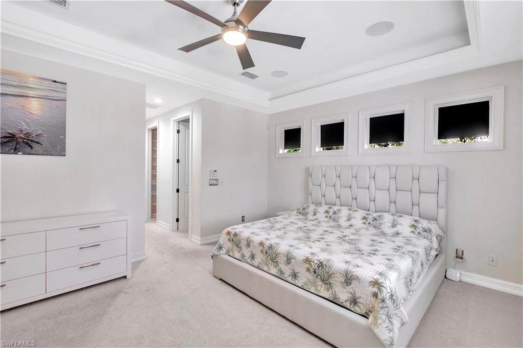 Spacious room featuring light-toned carpeting, a tray ceiling with crown molding, and a modern ceiling fan