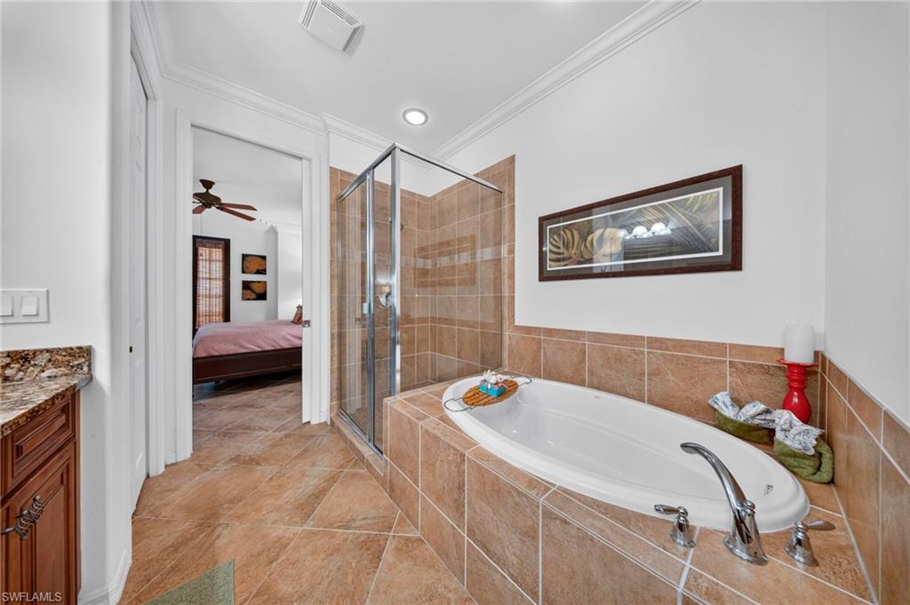 Tiled bathroom featuring a built-in soaking tub, a clear glass shower enclosure, and a vanity with a stone countertop