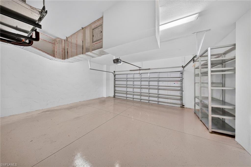 Spacious garage featuring a neutral-toned epoxy floor, white painted walls, a sectional garage door, and built-in metal shelving