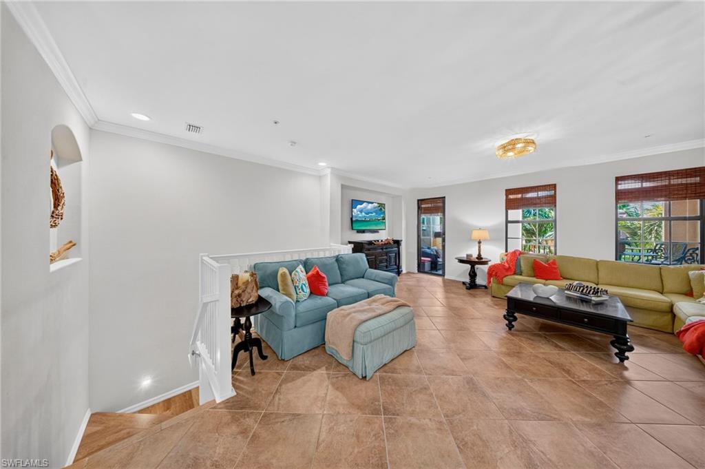 Spacious living area featuring tile flooring, white crown molding, recessed lighting, and a decorative arched wall niche