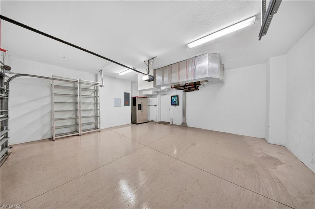 Spacious garage featuring a light-colored epoxy-coated concrete floor, bright overhead fluorescent lighting, built-in metal shelving, and a white interior door
