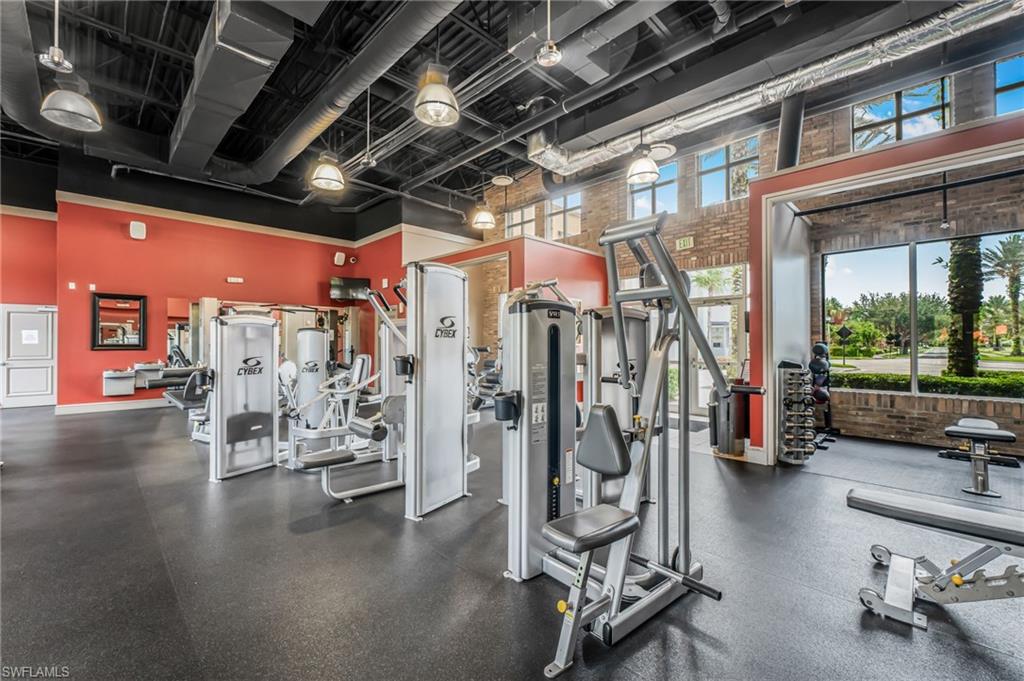 Fitness center featuring a rubberized floor, exposed ductwork, brick accents, large windows, and a variety of exercise equipment