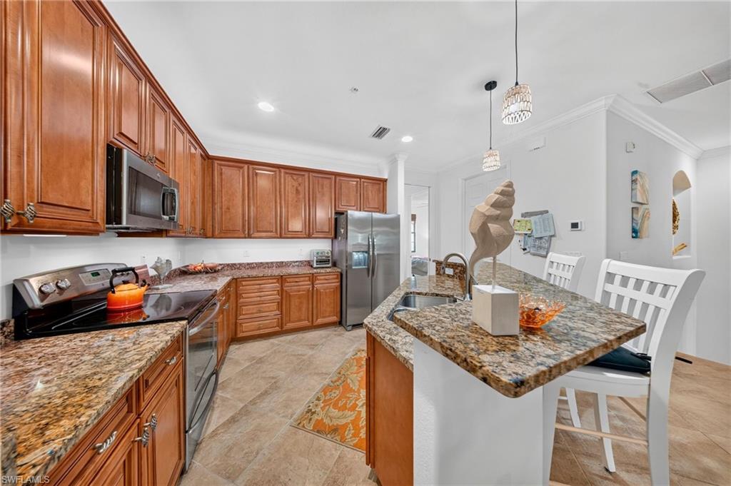 Kitchen featuring warm wood cabinetry, stainless steel appliances, speckled stone countertops, a breakfast bar, and tile flooring