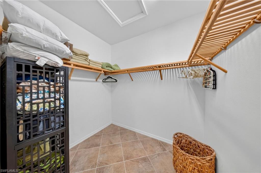 Walk-in closet featuring L-shaped wood shelving and tile flooring