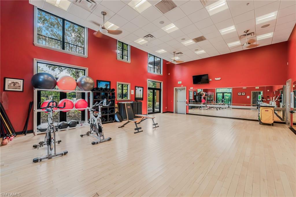 Spacious recreation room featuring light wood-finish flooring, vibrant red walls, and a dropped ceiling with recessed lighting