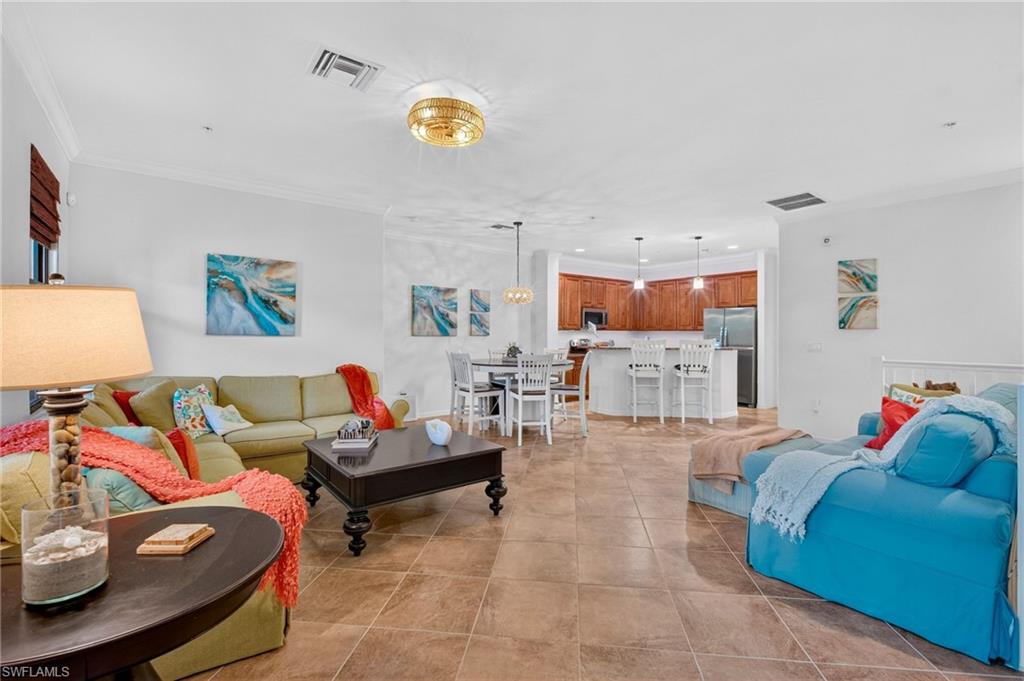 Open-concept living space featuring ceramic tile flooring, crown molding, a recessed ceiling, and a kitchen with wood cabinetry and stainless steel appliances