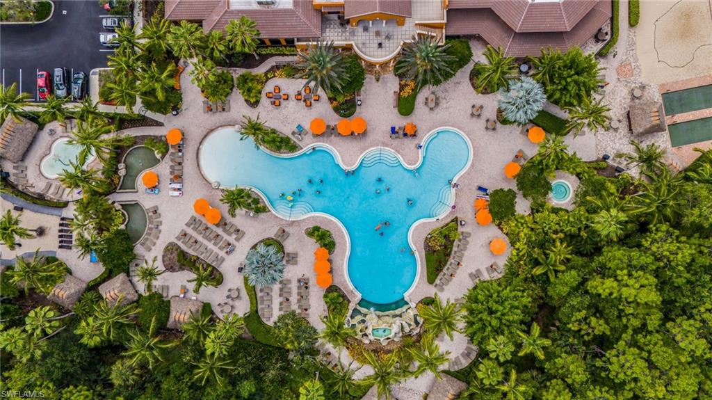 Expansive resort-style pool area featuring a freeform swimming pool, multiple lounging zones with umbrellas, lush tropical landscaping, a secondary pool with a waterfall feature, and an integrated spa