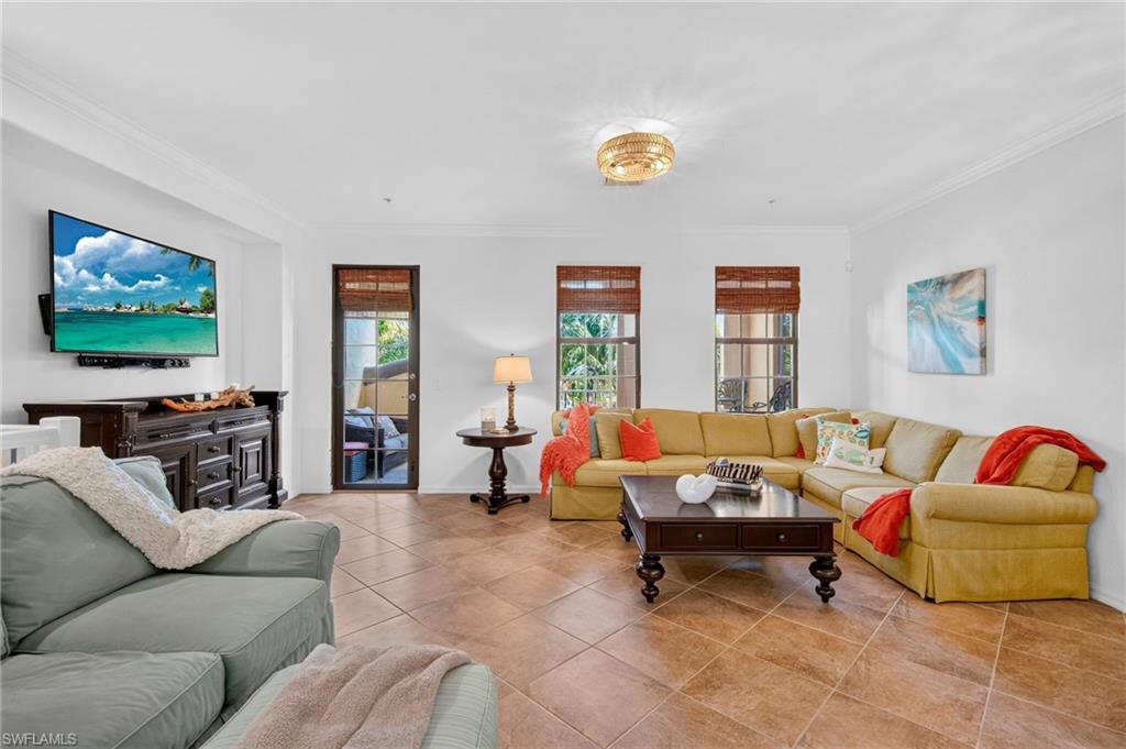 Living room featuring expansive tile flooring, crown molding, and multiple windows with woven wood shades