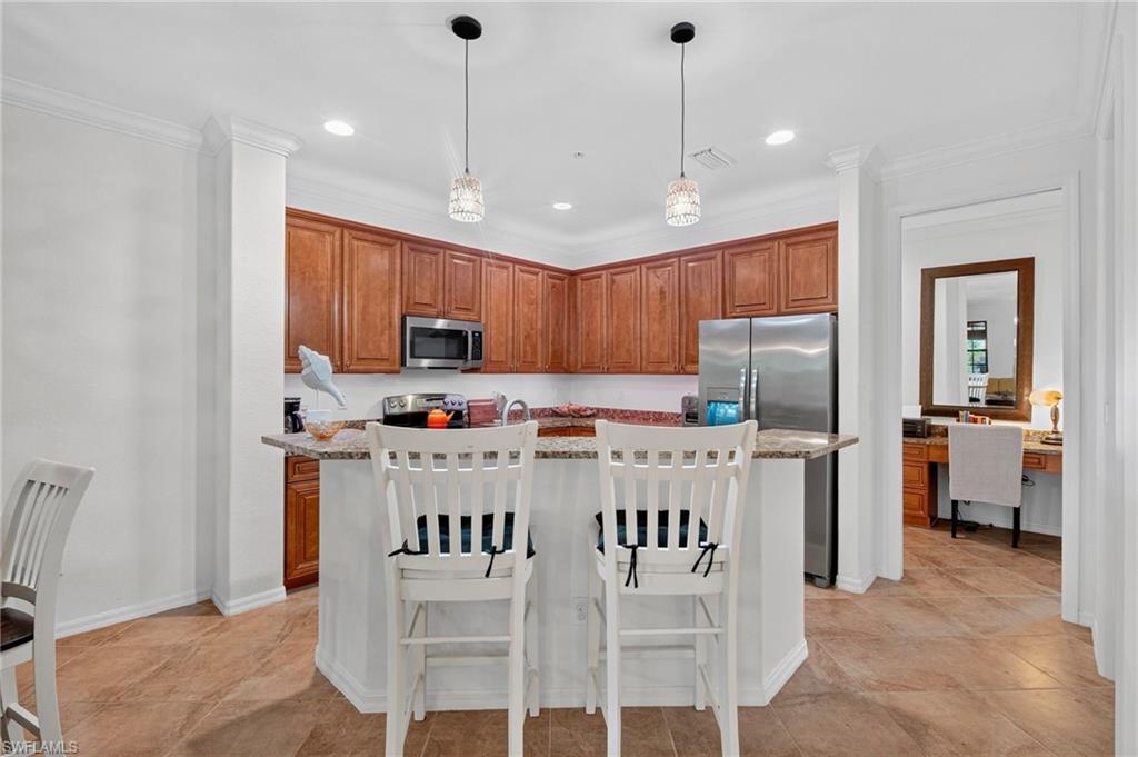 Kitchen featuring wood cabinetry, stainless steel appliances, and a breakfast bar with stone-finish countertops