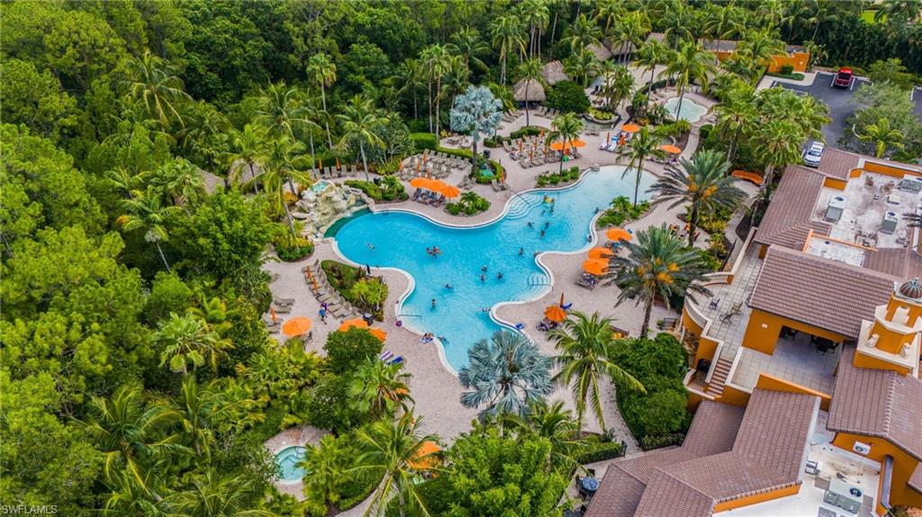 Expansive resort-style pool area featuring a freeform swimming pool, multiple lounging areas with umbrellas, lush tropical landscaping, a spa, and a grotto-style rock waterfall