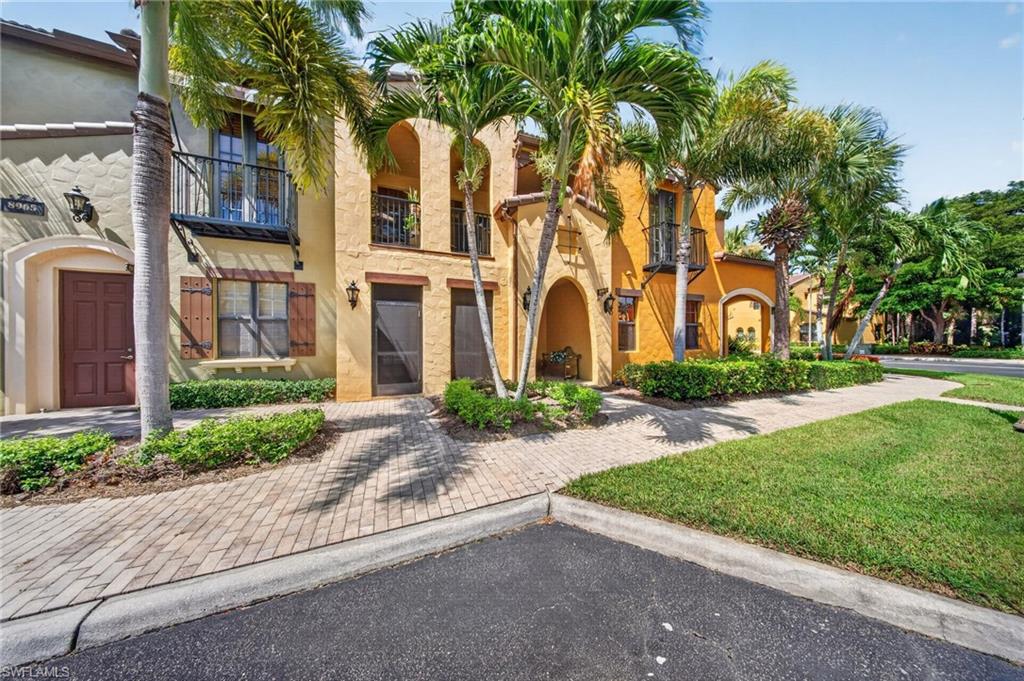 Mediterranean-style townhome with stucco exterior, arched entryways, private balconies with iron railings, and decorative window shutters
