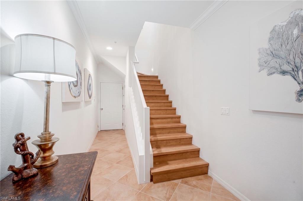 Entryway featuring light-toned tile flooring, a wood-finish staircase with white risers and railing, a white paneled door, and crown molding