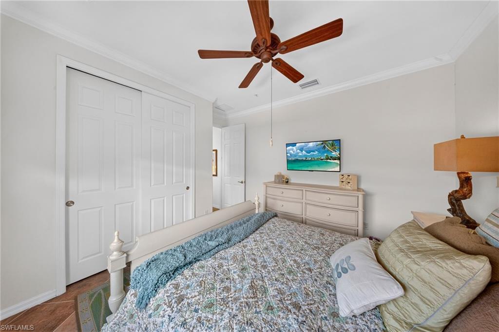 Wood-finish flooring with a decorative area rug, white bi-fold closet doors, crown molding, and a ceiling fan with wood-look blades