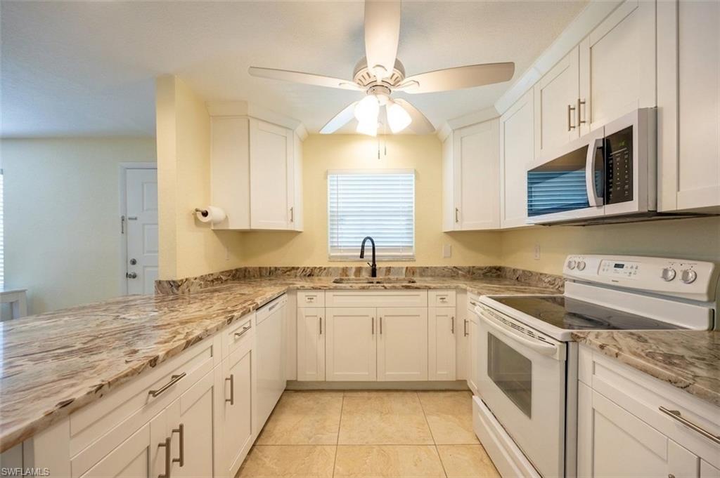U-shaped kitchen featuring white cabinetry, stone countertops, a ceiling fan, tiled flooring, and a built-in microwave