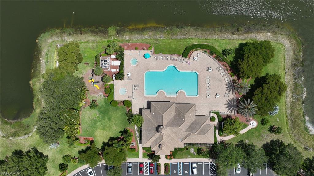 Expansive community amenities featuring a large resort-style pool with integrated spa areas, a spacious paved sundeck, lush green spaces with mature trees, and a dedicated playground area, all bordered by a tranquil water feature