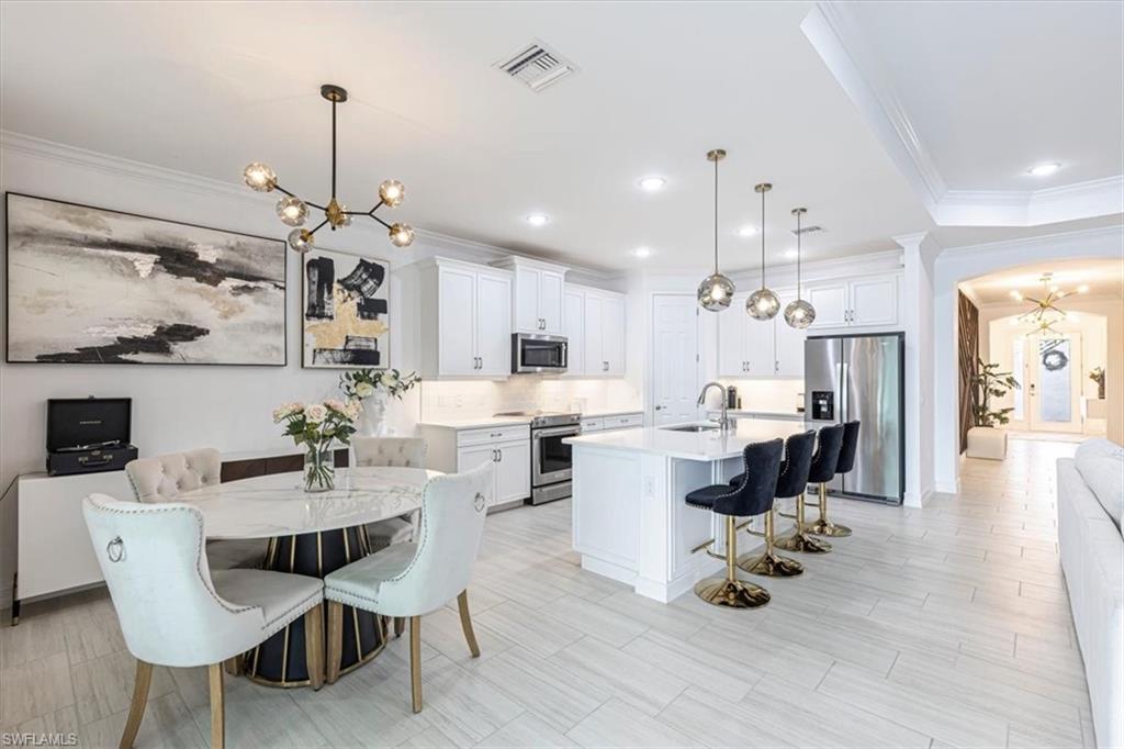 Kitchen featuring a chandelier, ornamental molding, a kitchen bar, stainless steel appliances, and white cabinetry