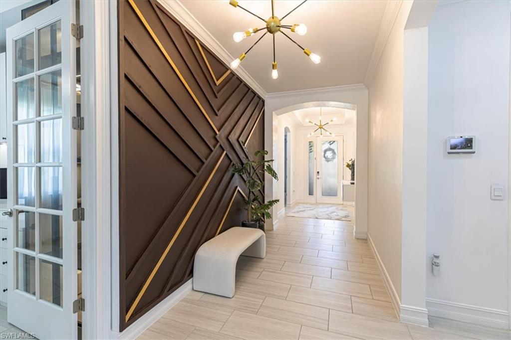 Entryway with crown molding, a chandelier, wood finish floors, and arched walkways