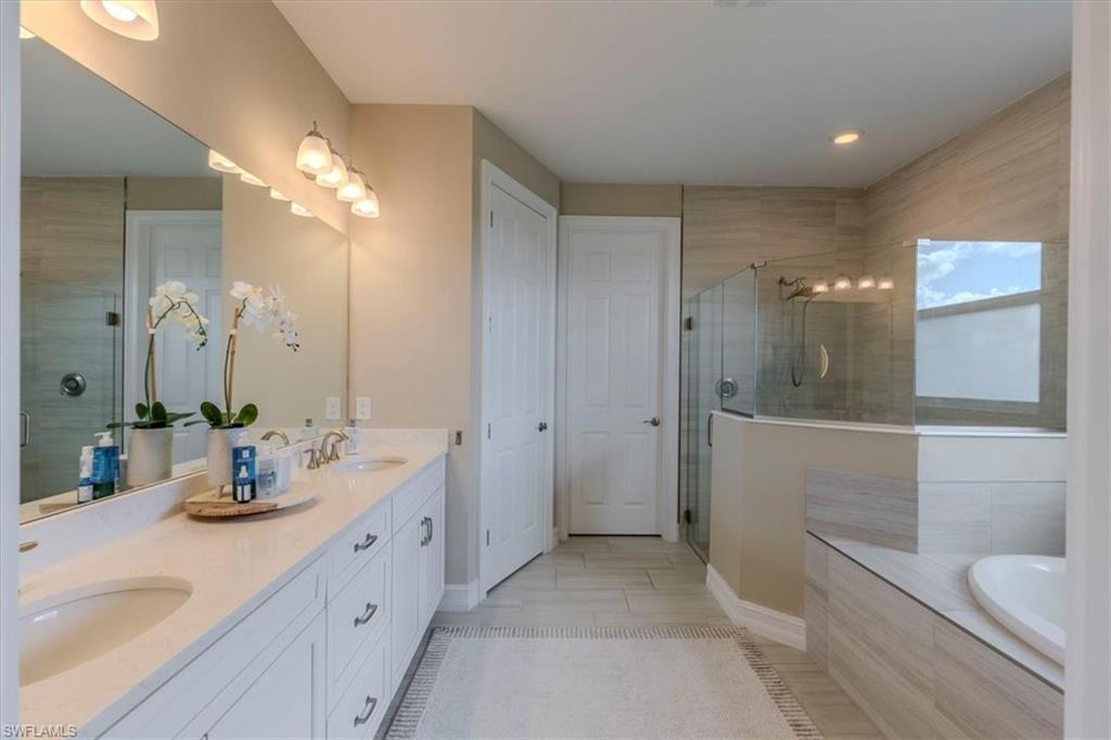 Full bathroom featuring double vanity, a stall shower, and tiled bath
