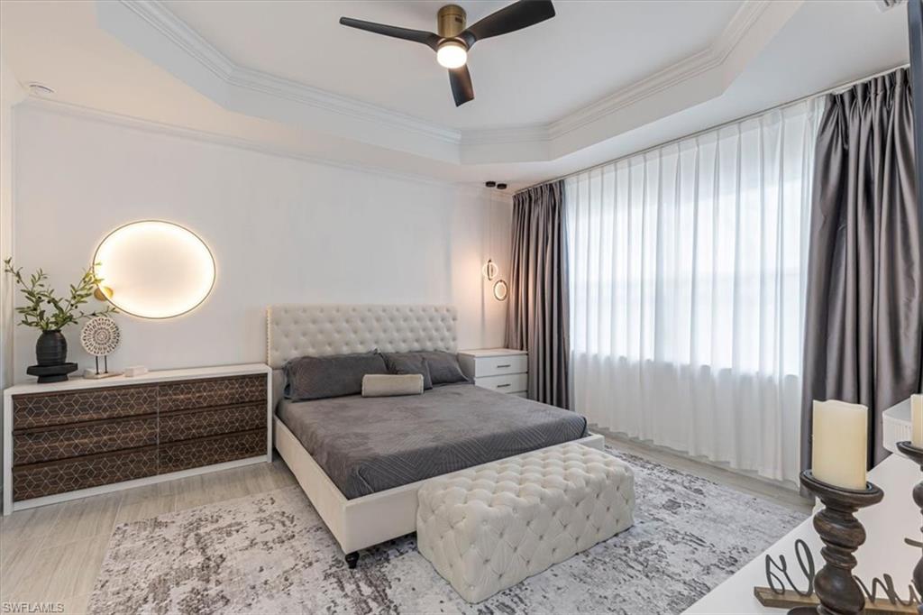 Bedroom with a raised ceiling, crown molding, a ceiling fan, and light wood-type flooring