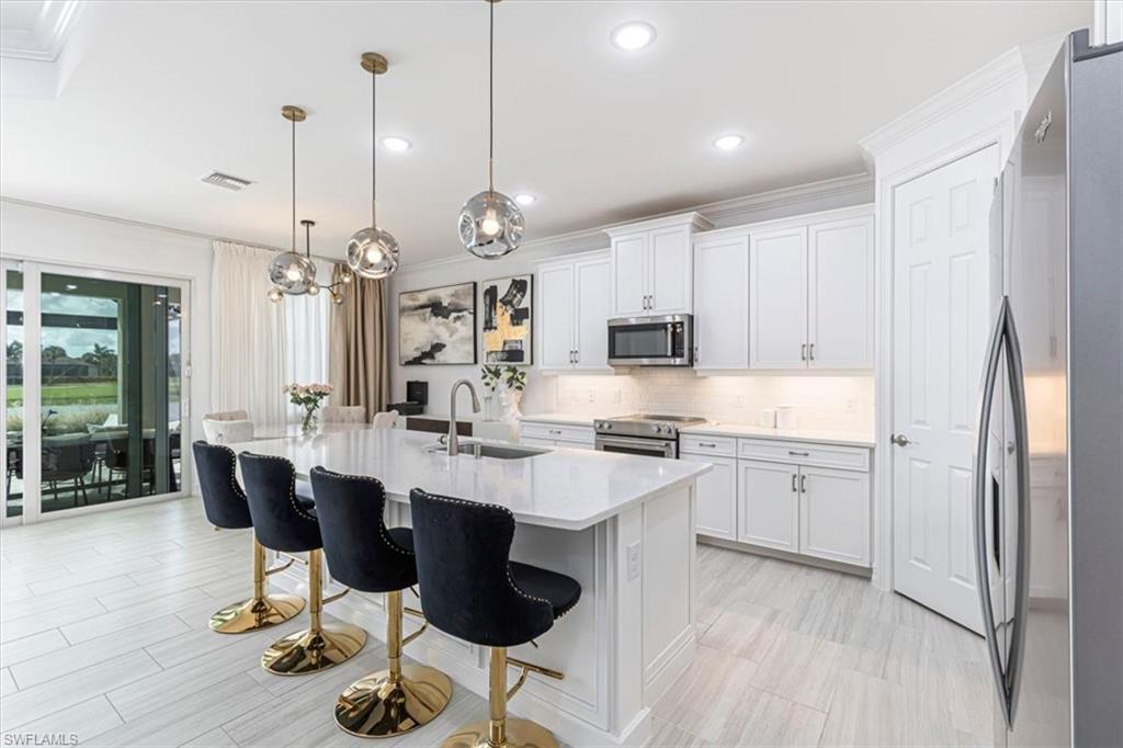 Kitchen featuring crown molding, stainless steel appliances, hanging light fixtures, a kitchen island with sink, and a breakfast bar