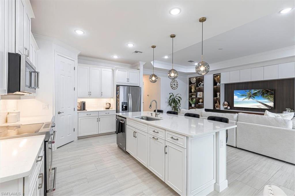 Kitchen with ornamental molding, decorative light fixtures, open floor plan, white cabinets, and stainless steel appliances