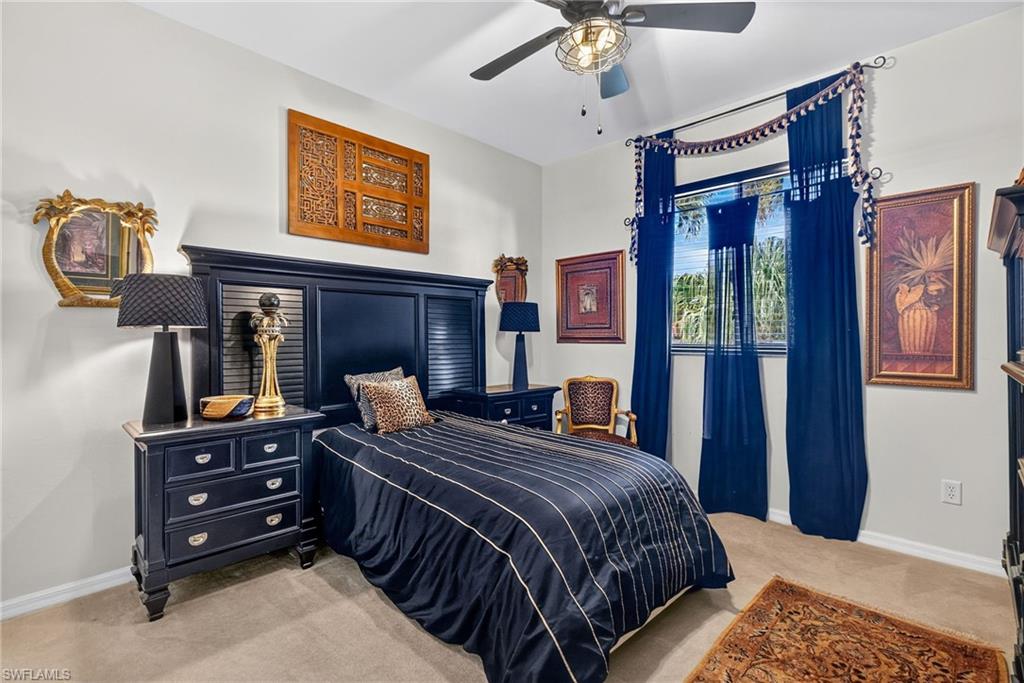 Carpeted bedroom featuring a window with blue sheer and solid drapes, a ceiling fan with integrated lighting, and light-toned walls