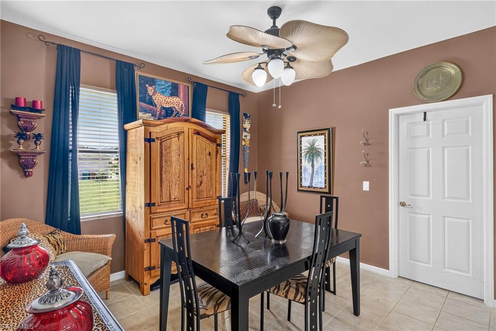 Dining area featuring neutral tile flooring, two windows with blinds and dark draperies, a multi-paneled white door, and a ceiling fan with light fixture