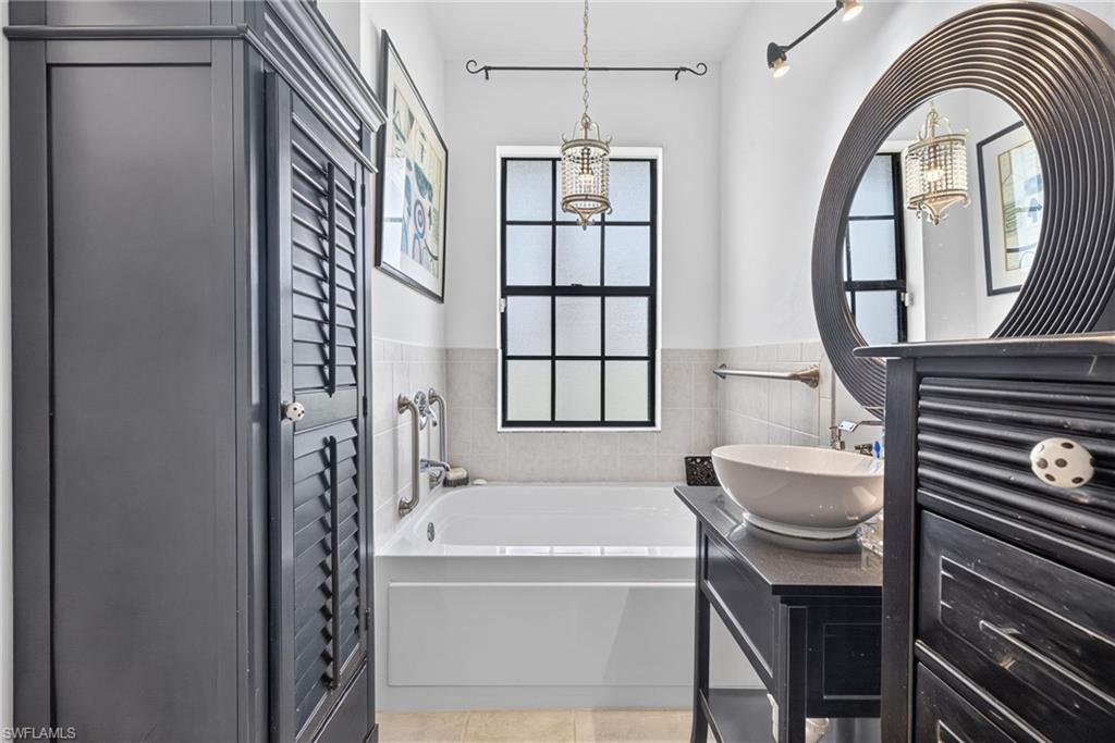 Bathroom featuring a soaking tub, a black grid window, and a vessel sink vanity with an ornate mirror